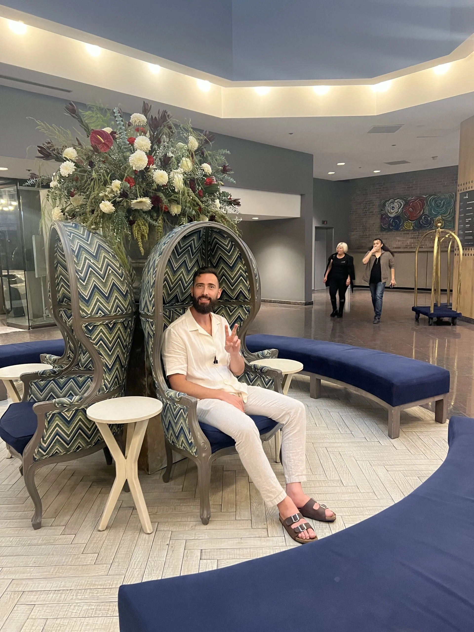 Gary Karen Shamoyan gesturing the peace sign from a chair in the lobby while on vacation